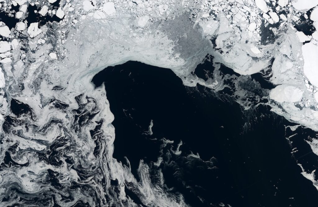 Satellite view of the Arctic Ocean: fragmented white sea-ice floes drifting over dark, swirling ocean water